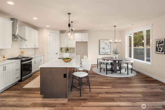 kitchen featuring gas range, wall chimney exhaust hood, a breakfast bar area, dark wood-style flooring, and white cabinetry