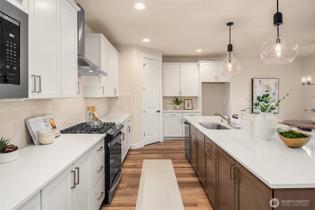 kitchen with light wood-style floors, a sink, black gas stove, wall chimney range hood, and stainless steel dishwasher