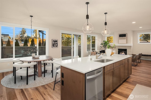 kitchen with a sink, open floor plan, a lit fireplace, light wood-type flooring, and dishwasher