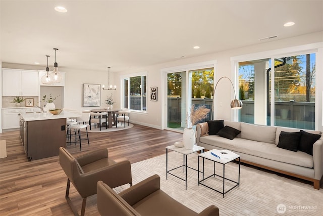 living area featuring baseboards, visible vents, light wood-style flooring, a notable chandelier, and recessed lighting