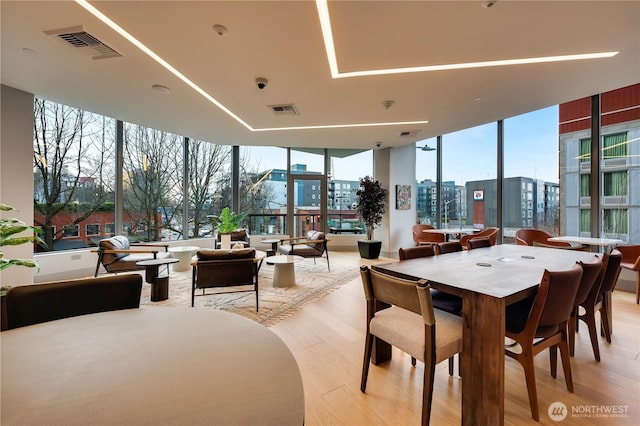 dining space featuring light wood-style floors, a view of city, visible vents, and a wall of windows