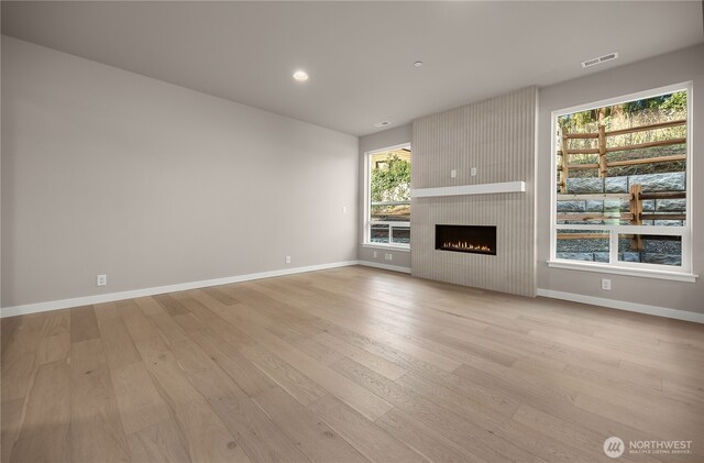 unfurnished living room featuring baseboards, visible vents, and light wood-style floors