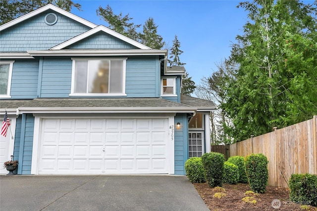 view of front of house with driveway, an attached garage, fence, and roof with shingles