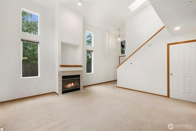unfurnished living room featuring baseboards, a fireplace, a towering ceiling, and light colored carpet