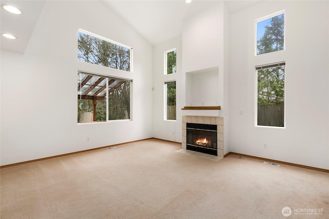 unfurnished living room with baseboards, visible vents, light colored carpet, a fireplace, and high vaulted ceiling