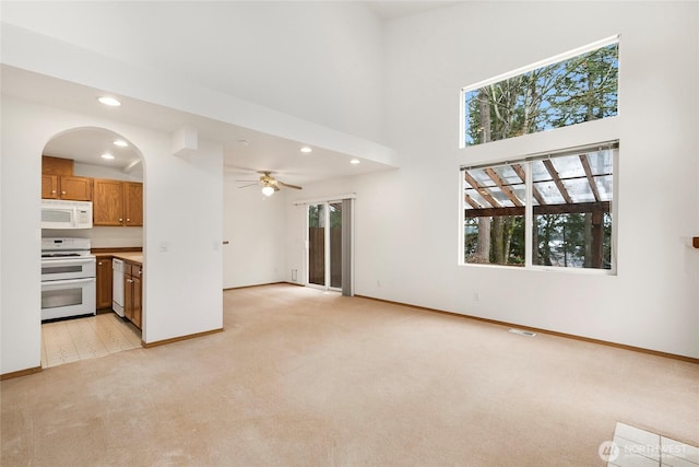 unfurnished living room with recessed lighting, light colored carpet, a towering ceiling, and baseboards