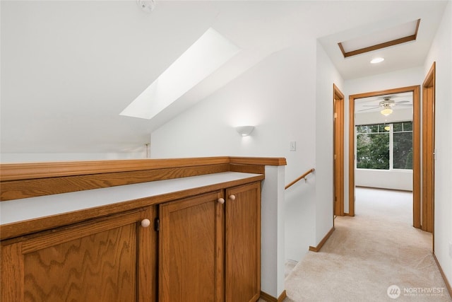 hallway with light carpet, lofted ceiling with skylight, an upstairs landing, and baseboards