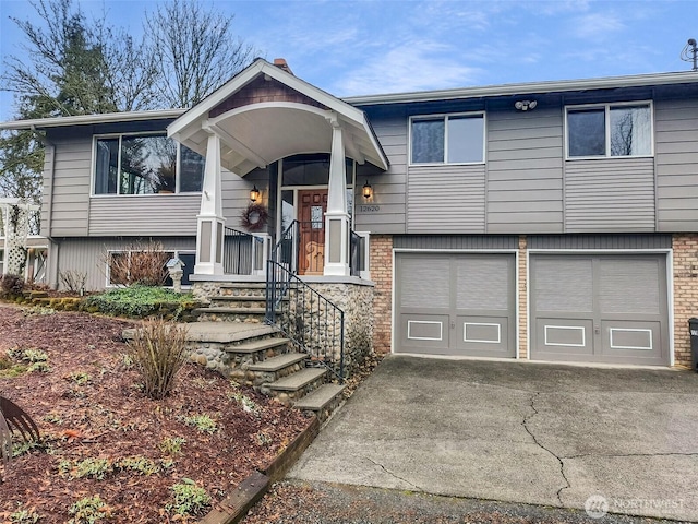 raised ranch with a garage, driveway, and brick siding