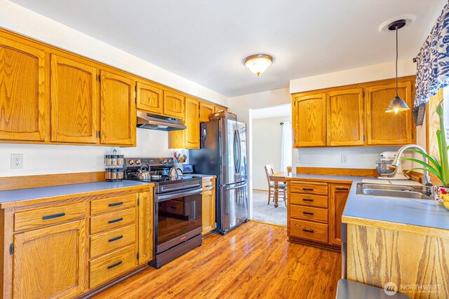 kitchen with appliances with stainless steel finishes, brown cabinets, decorative light fixtures, and under cabinet range hood