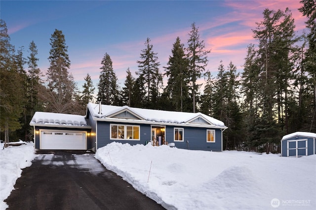 view of front of house with an attached garage, a storage shed, and aphalt driveway