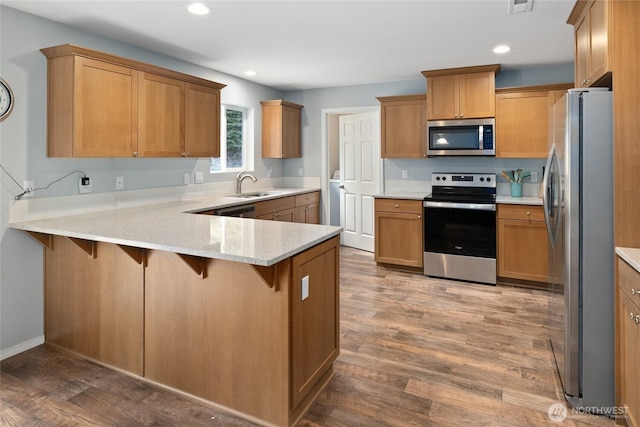 kitchen featuring recessed lighting, a peninsula, appliances with stainless steel finishes, a sink, and wood finished floors