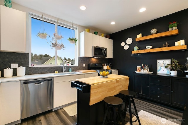 kitchen with a breakfast bar, a sink, white cabinets, appliances with stainless steel finishes, and dark wood-style floors