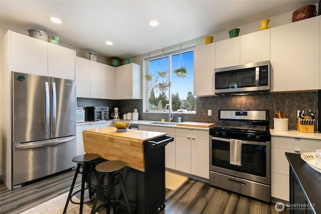 kitchen with decorative backsplash, a center island, stainless steel appliances, white cabinetry, and a sink