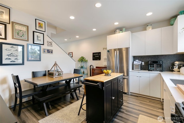 kitchen featuring a kitchen island, white cabinets, light countertops, dark cabinetry, and freestanding refrigerator