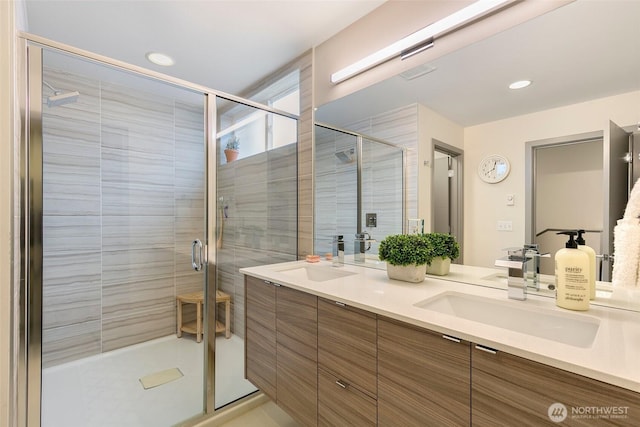 bathroom featuring double vanity, a stall shower, a sink, and recessed lighting