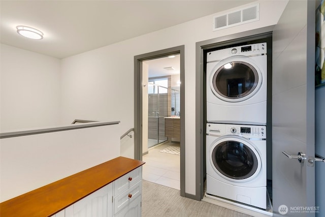 laundry area with stacked washer / dryer, laundry area, visible vents, and light tile patterned floors