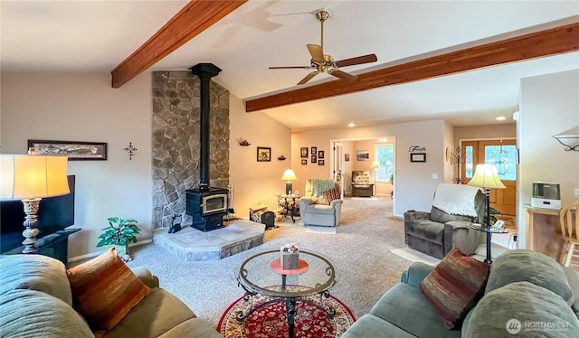 carpeted living room with a wood stove, vaulted ceiling with beams, and ceiling fan