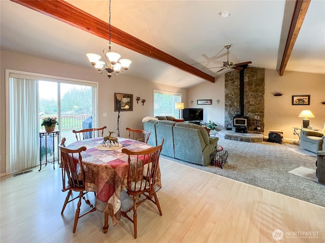 dining room with vaulted ceiling with beams, light wood finished floors, visible vents, a ceiling fan, and a wood stove