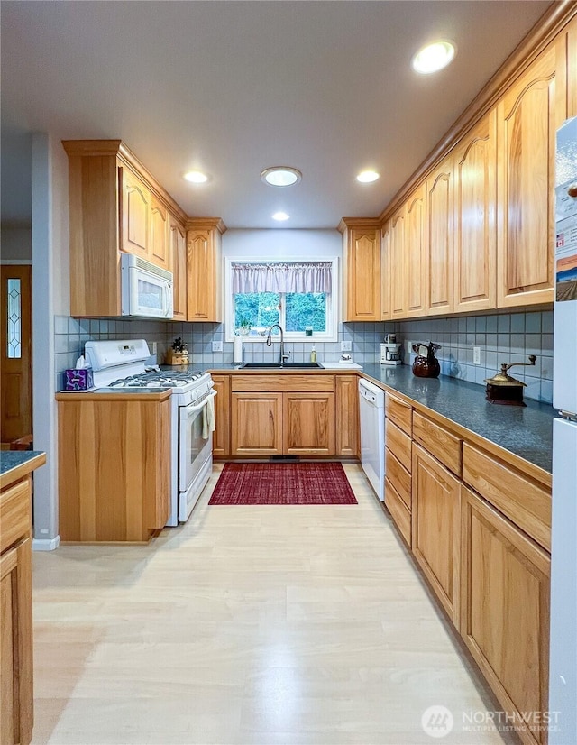 kitchen with white appliances, tasteful backsplash, dark countertops, light wood-style floors, and a sink