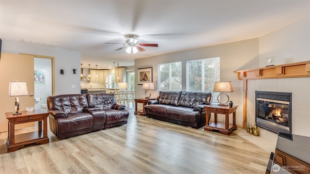 living room featuring light wood-type flooring, visible vents, ceiling fan, and a tiled fireplace