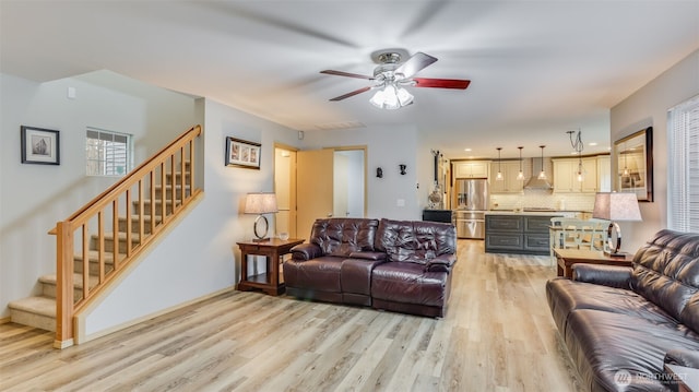 living area with light wood-type flooring, ceiling fan, stairway, and baseboards