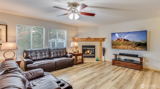 living area featuring light wood-style floors, baseboards, a ceiling fan, and a tiled fireplace