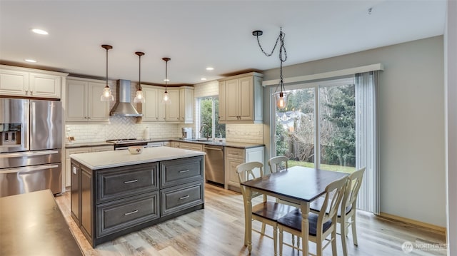 kitchen featuring wall chimney exhaust hood, appliances with stainless steel finishes, a center island, hanging light fixtures, and light countertops