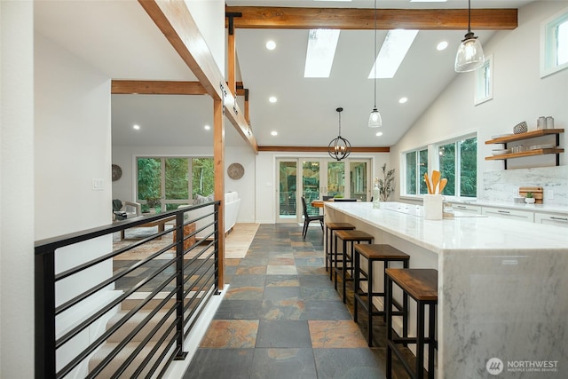 kitchen featuring light stone counters, stone tile floors, a breakfast bar, white cabinets, and pendant lighting