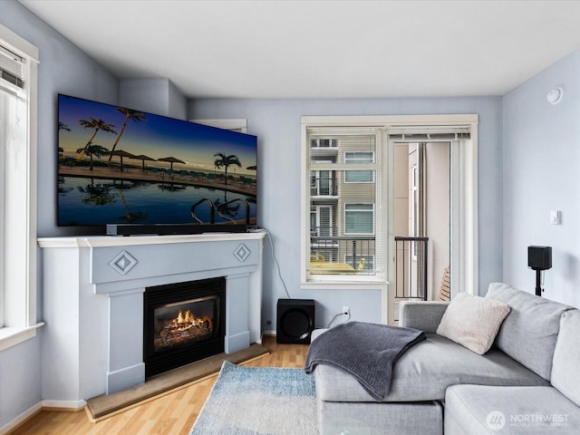 living area with light wood-style floors, baseboards, and a glass covered fireplace