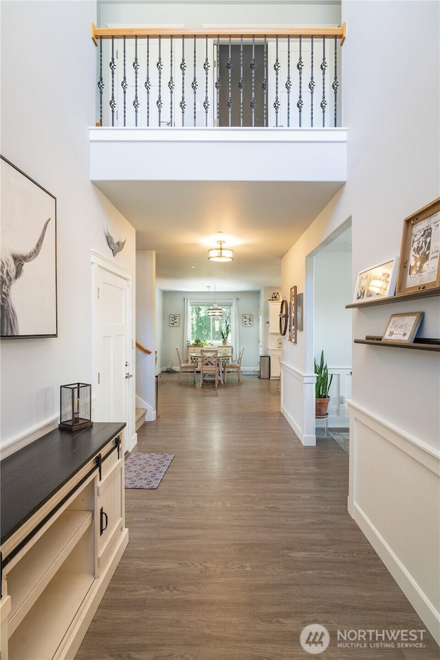 corridor with a towering ceiling, baseboards, and dark wood-type flooring