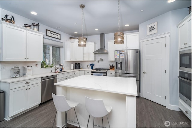 kitchen with stainless steel appliances, white cabinets, decorative light fixtures, and wall chimney range hood