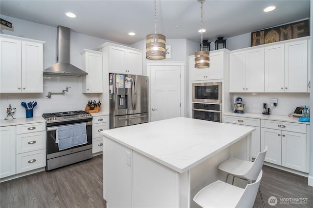 kitchen with decorative light fixtures, stainless steel appliances, dark wood-type flooring, white cabinets, and wall chimney exhaust hood