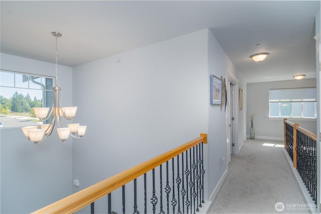 hallway featuring light carpet, an inviting chandelier, baseboards, and an upstairs landing