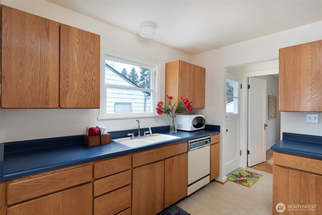 kitchen with dark countertops, a sink, brown cabinetry, and dishwasher