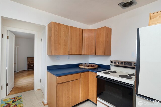 kitchen featuring range with electric stovetop, dark countertops, visible vents, brown cabinetry, and freestanding refrigerator