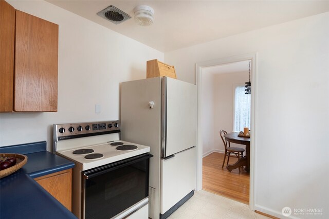 kitchen featuring white appliances, visible vents, brown cabinets, light floors, and dark countertops