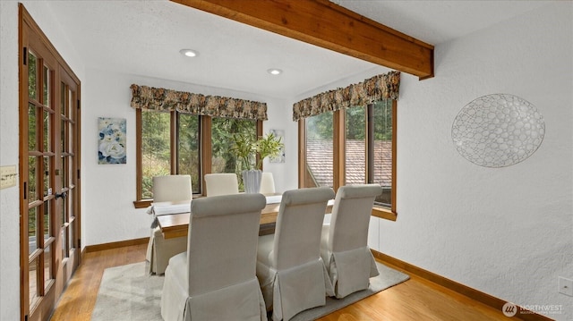 dining space with baseboards, a textured wall, light wood finished floors, and beam ceiling