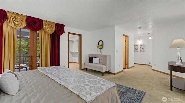 bedroom with a spacious closet, baseboards, a textured ceiling, and light colored carpet