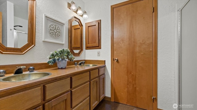 full bathroom with double vanity, a sink, and a textured wall