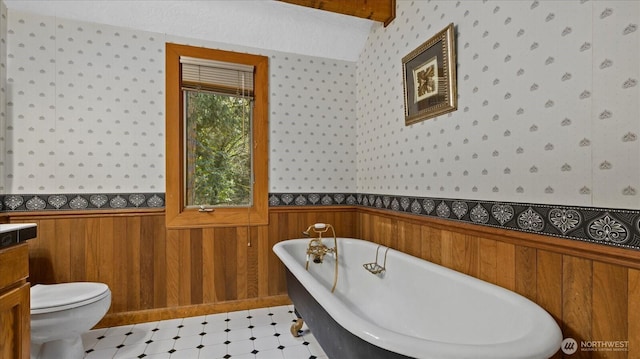 bathroom with wallpapered walls, toilet, a wainscoted wall, a freestanding bath, and vanity