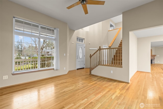 entrance foyer with light wood-type flooring, stairs, a fireplace, and a ceiling fan