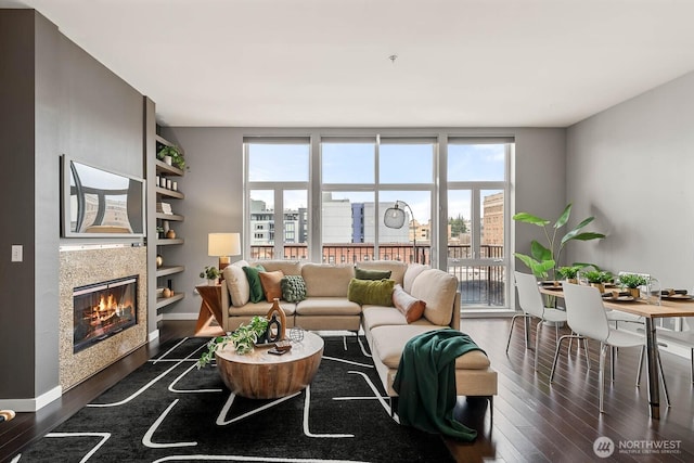 living room featuring dark wood-type flooring, a fireplace, built in shelves, and baseboards