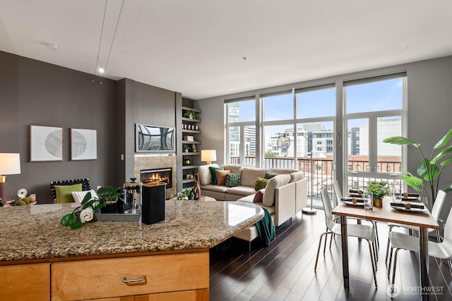 kitchen featuring stone countertops, open floor plan, dark wood finished floors, and a glass covered fireplace