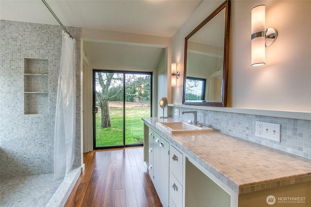 bathroom featuring curtained shower, wood finished floors, vanity, and backsplash