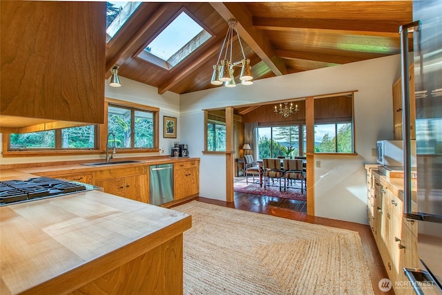 kitchen featuring lofted ceiling with skylight, dishwasher, a sink, brown cabinetry, and a notable chandelier