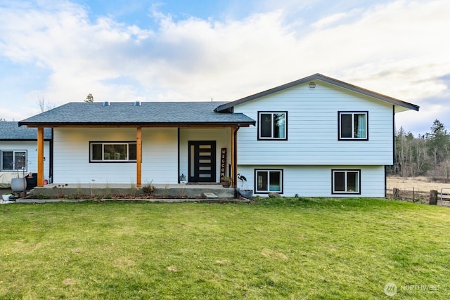 tri-level home featuring a front lawn, a shingled roof, and fence