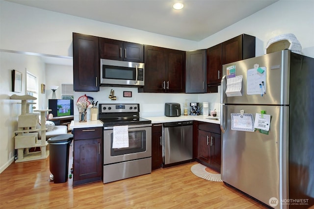 kitchen with dark brown cabinets, stainless steel appliances, and light hardwood / wood-style flooring