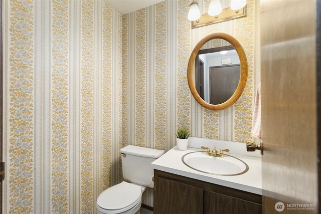 half bathroom with toilet, wallpapered walls, and vanity