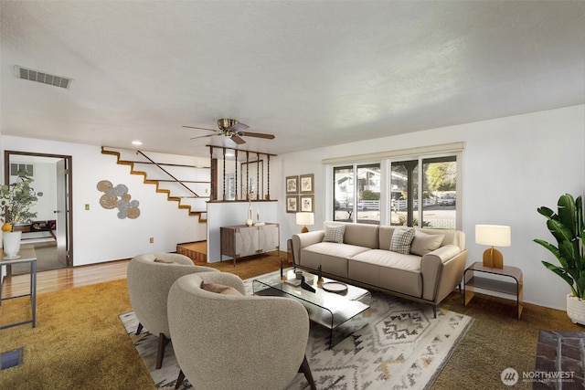 living area with a ceiling fan, visible vents, and stairs