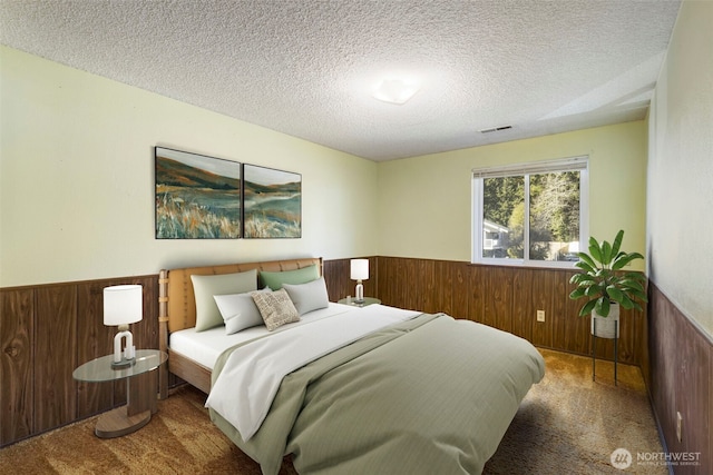 bedroom featuring wooden walls, visible vents, wainscoting, a textured ceiling, and carpet floors